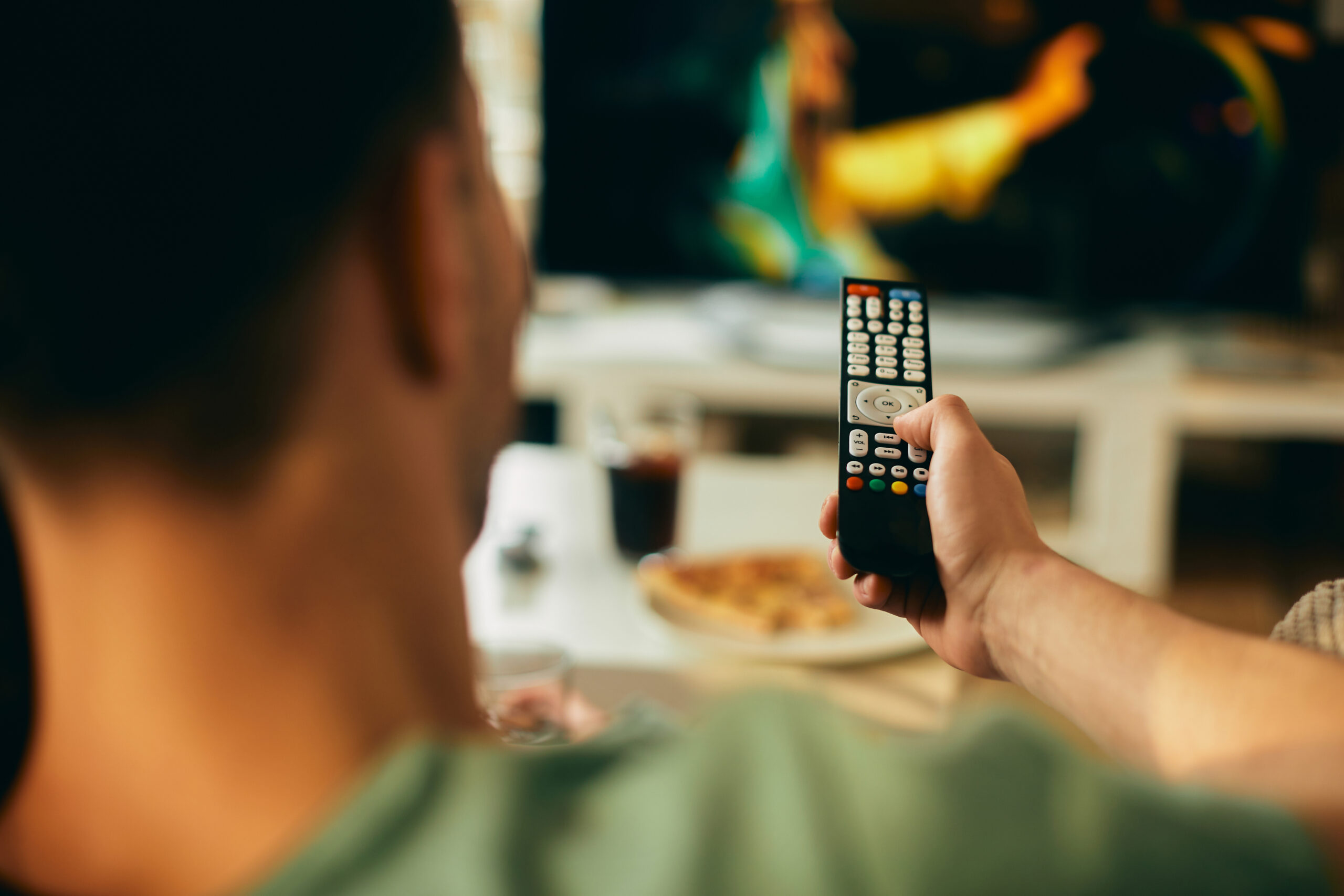 Foto van een jonge man die thuis tv kijkt met de afstandsbediening in zijn hand