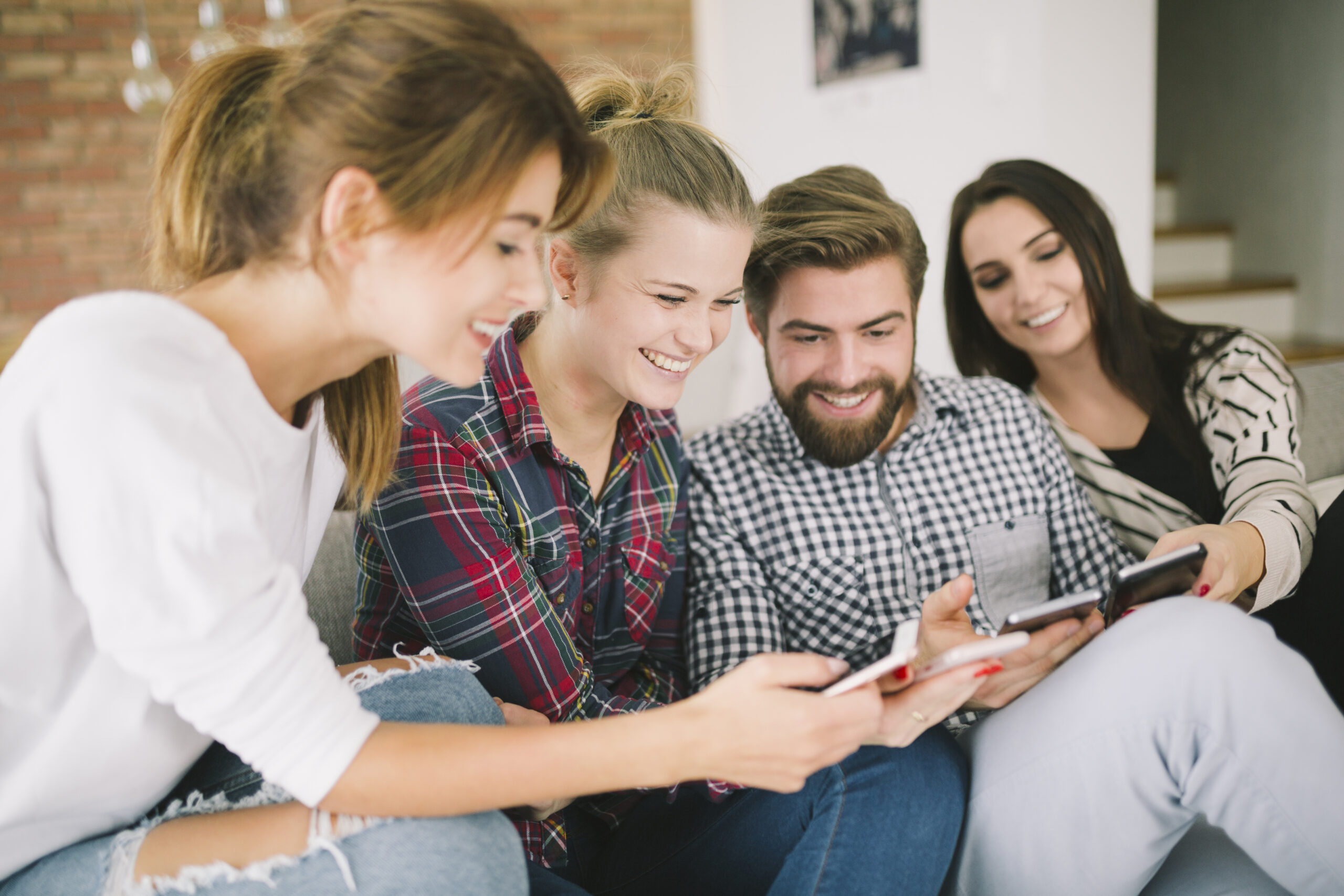 Photo of three young women and a young man sitting down, holding their mobile phones and comparing what’s on their screens